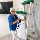 An older woman smiling while steadying a step ladder at home