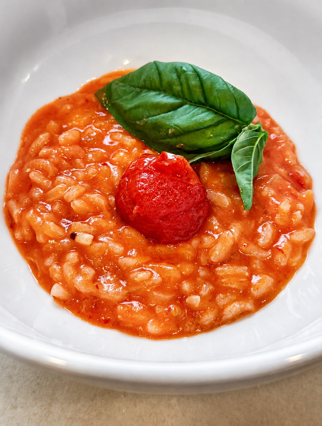 Summer Tomato Risotto in a white bowl, topped with a roasted tomato and fresh basil